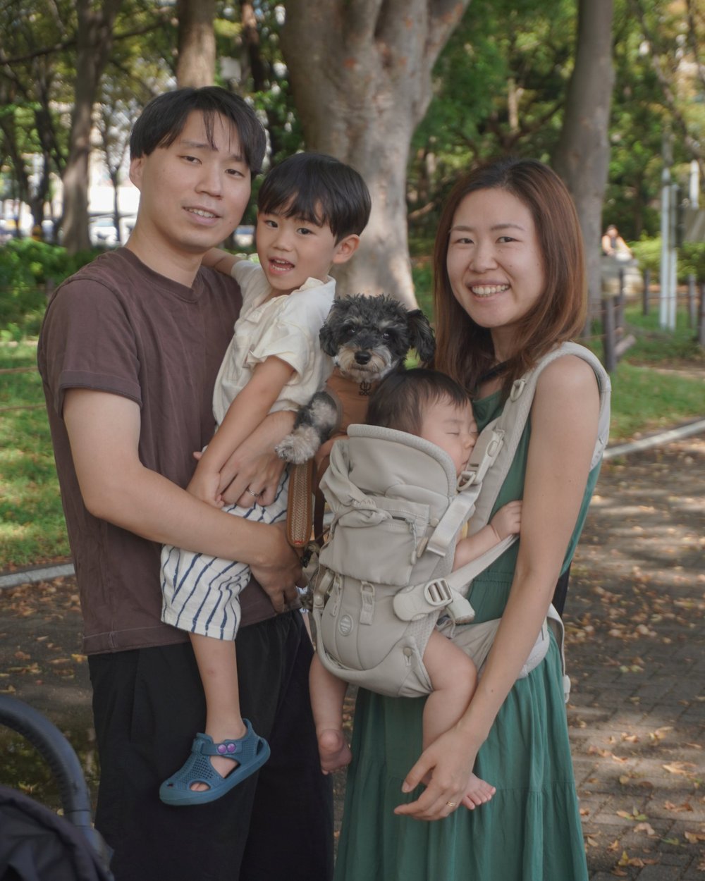 公園で寄り添って笑顔を見せる、お父さん、お母さん、男の子、赤ちゃん、愛犬の家族写真